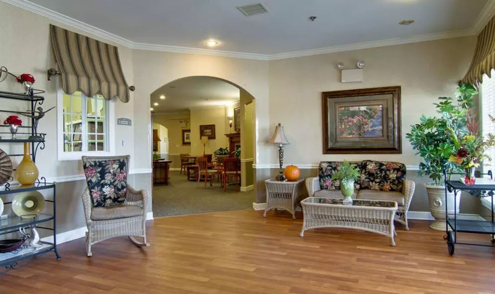 A cozy lobby area with wicker furniture and hardwood flooring, leading to another room through an archway.