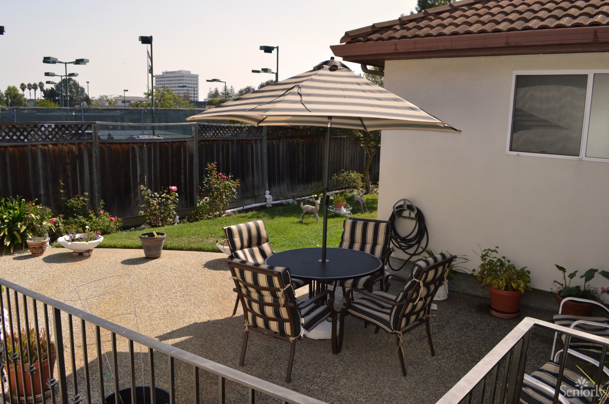 A cozy patio area with a table, chairs, and an umbrella in a garden setting.