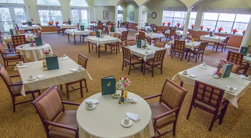 A spacious dining room with neatly arranged tables and chairs, featuring place settings and menus on each table.