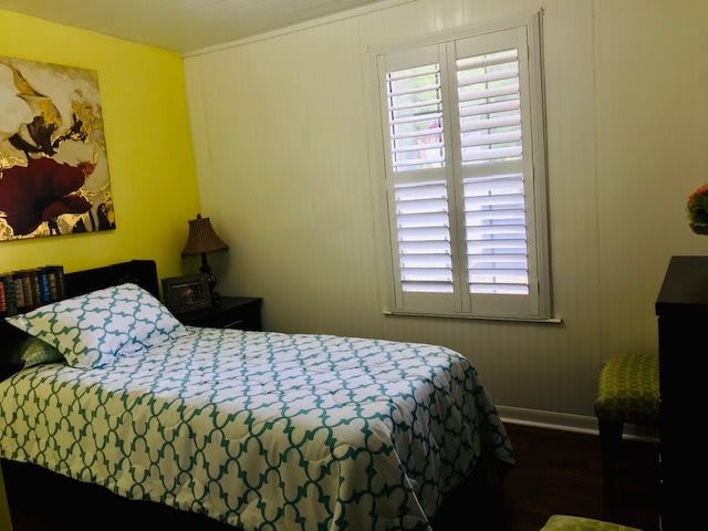A cozy bedroom with a bed, lamp, and window featuring shutters.