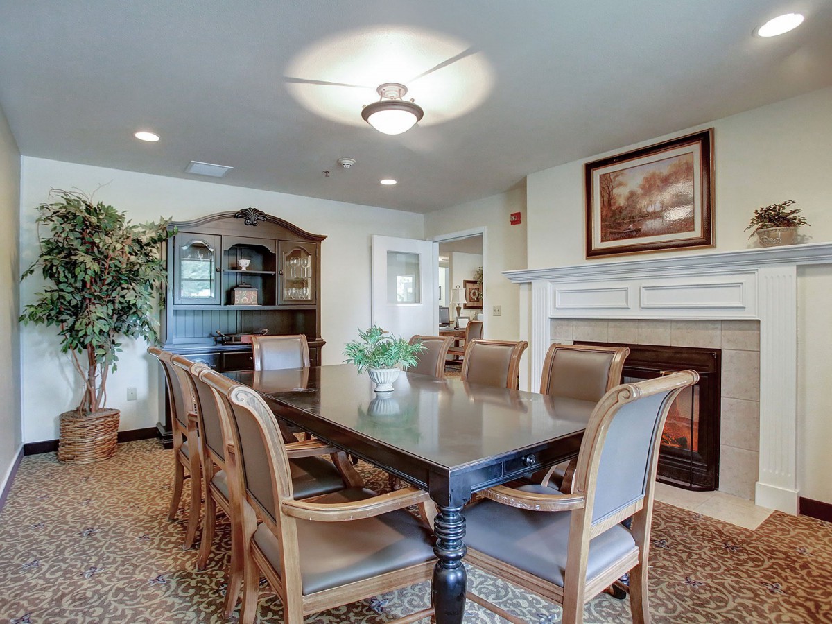 A cozy dining room with a large table, surrounded by chairs, featuring a fireplace and artwork on the wall.