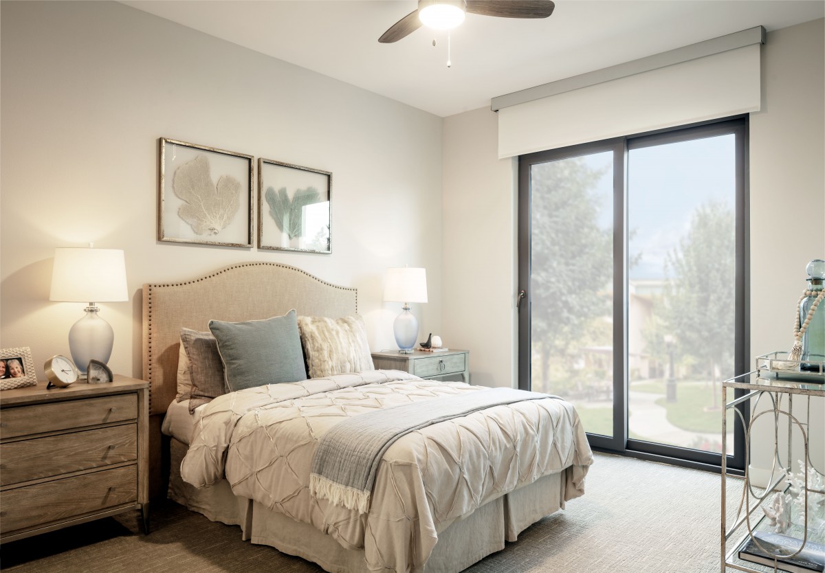 A modern bedroom with a cozy bed and soft lighting, featuring large windows and neutral color tones.