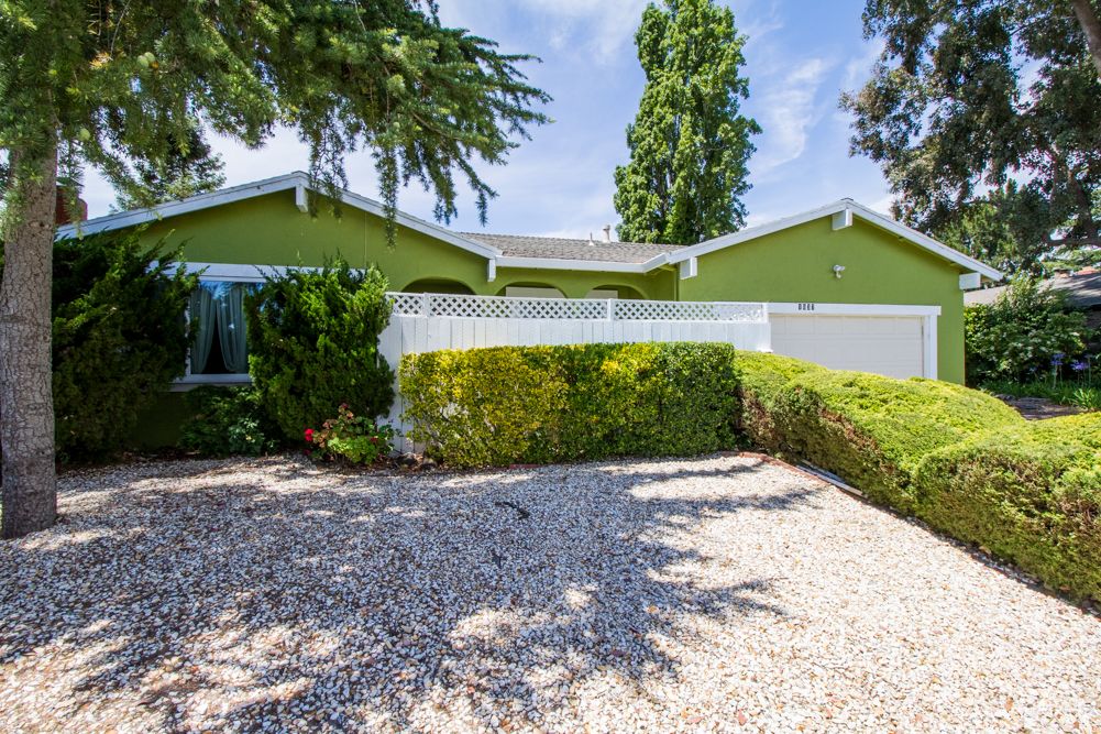 A charming single-story house with a green exterior and well-maintained front yard landscaping.