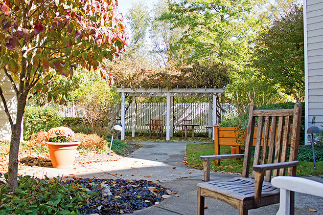 A serene garden setting with a pergola, chairs, and lush greenery.