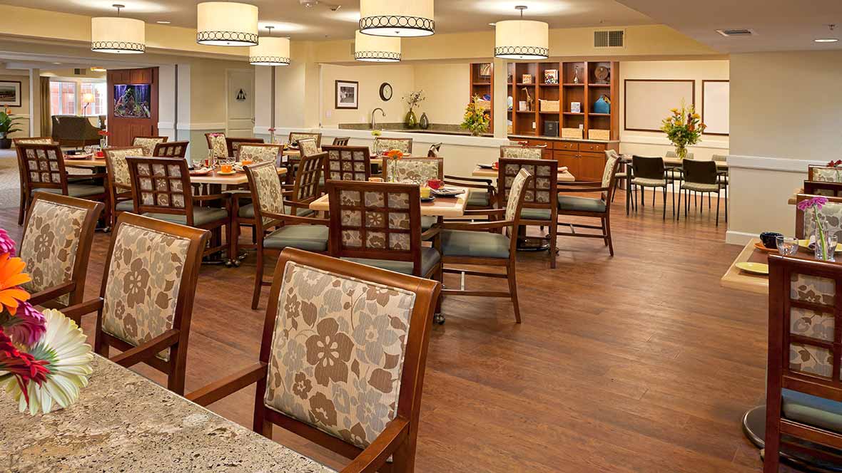 A cozy dining area with neatly arranged tables and chairs, featuring warm lighting and wooden flooring.