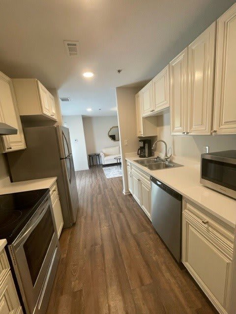A modern kitchen with white cabinets and wooden flooring, featuring various appliances and bright lighting.