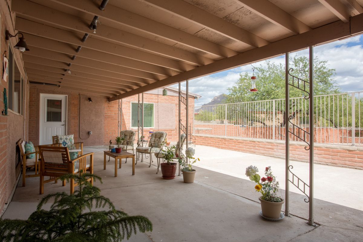 A cozy covered patio with chairs and potted plants, overlooking a desert landscape.