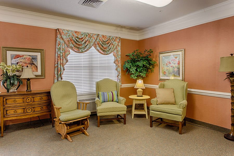 A cozy living room area with comfortable armchairs, a small lamp on a side table, and decorative curtains.