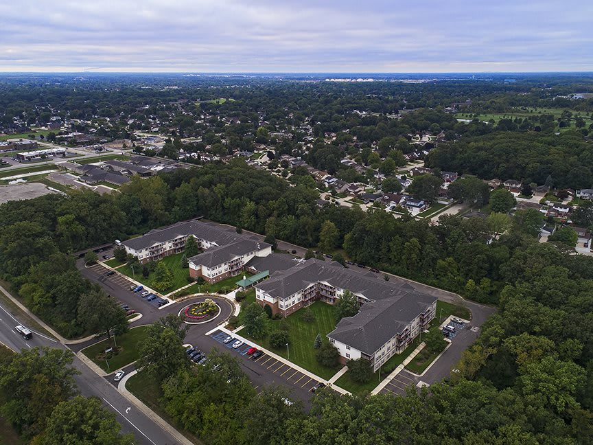Aerial view of a residential apartment complex surrounded by trees and a suburban neighborhood.