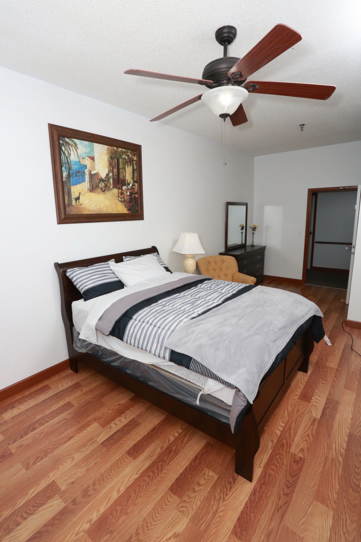 A cozy bedroom with a neatly made bed, a painting on the wall, and wooden flooring.