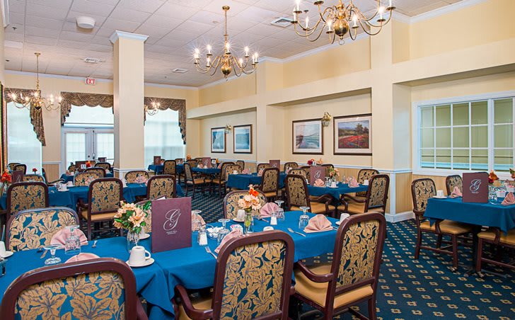 An elegant dining room with tables set for guests, featuring chandeliers and decorative art on the walls.