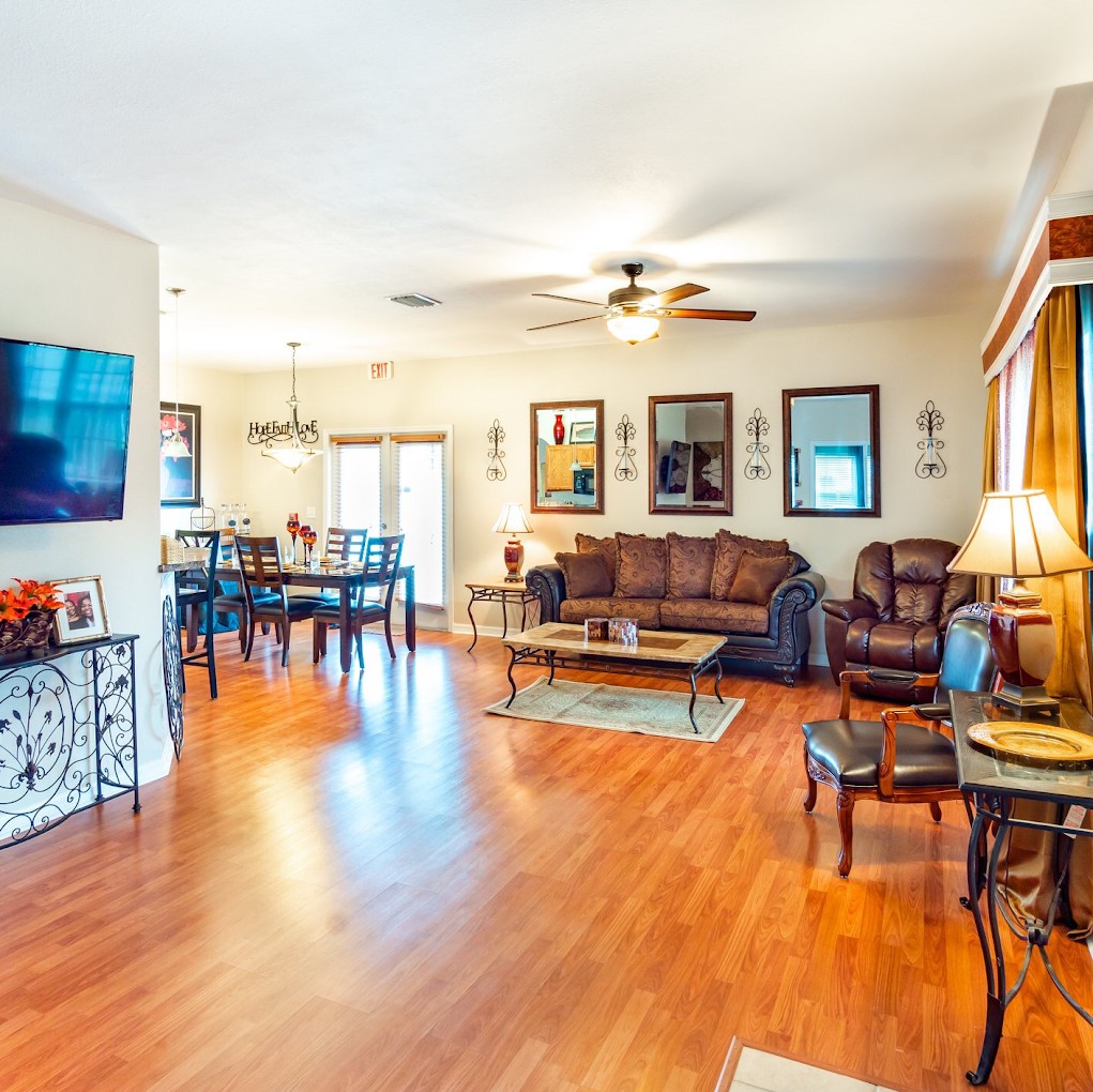 A spacious living room with a connected dining area features hardwood flooring, warm lighting, and stylish decor.