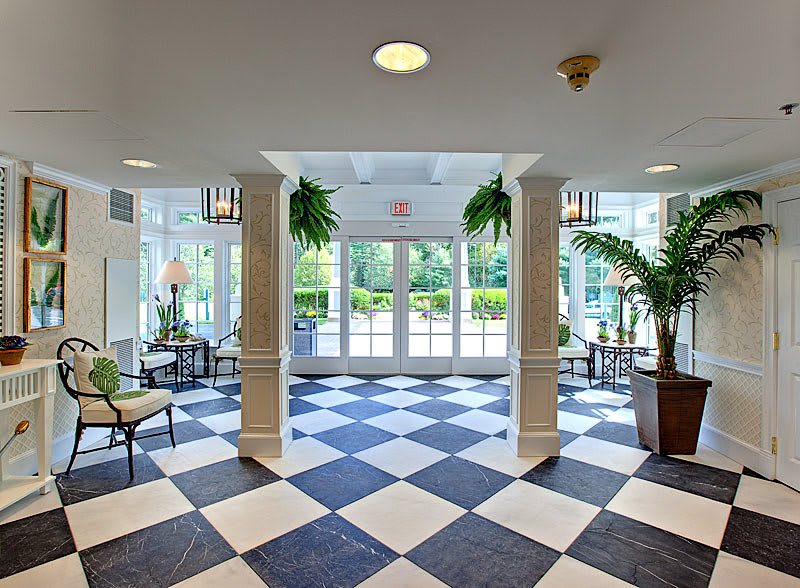 A well-lit lobby featuring black and white checkered floor tiles, lush plants, and comfortable seating areas.