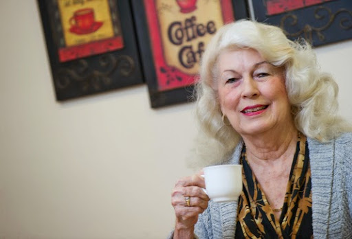 An elderly woman enjoying a cup of coffee with a warm smile.
