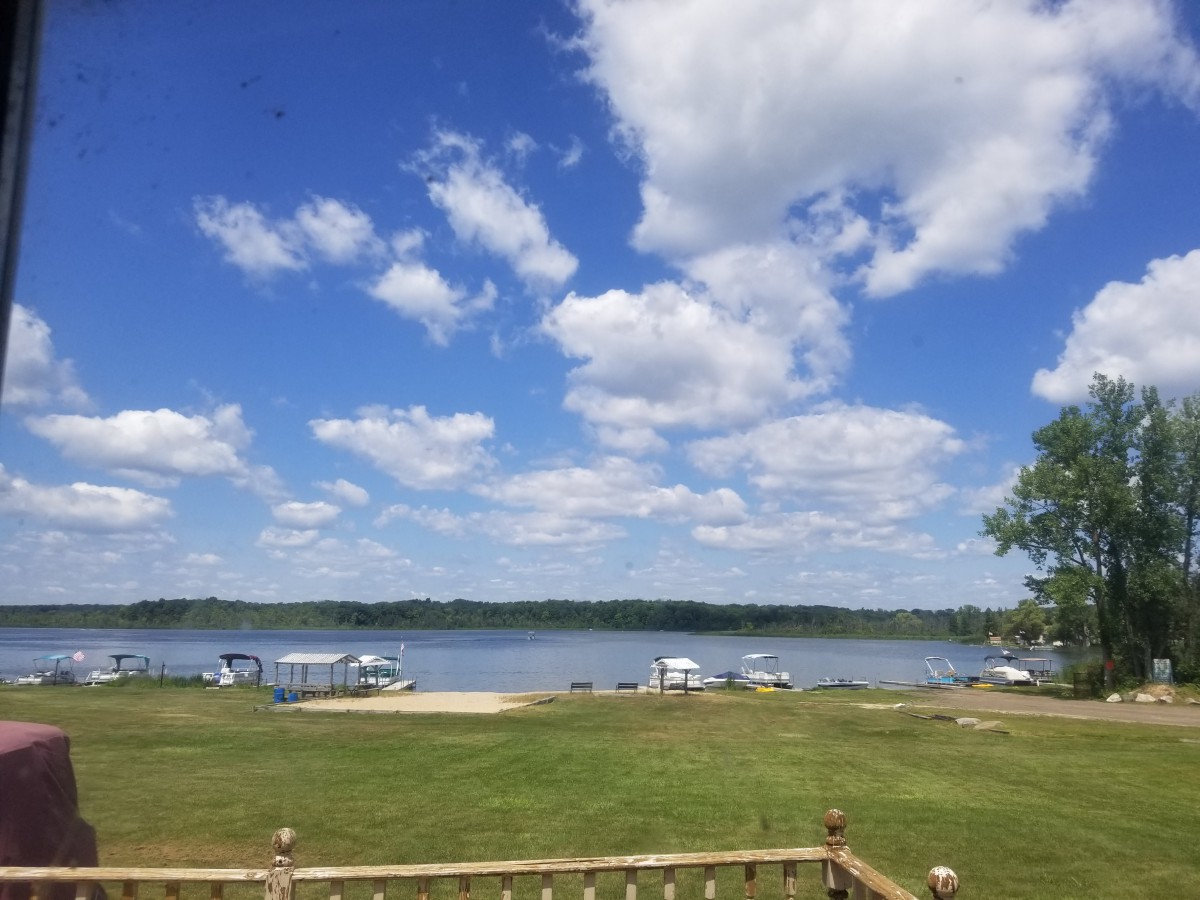 A scenic view of a lake with boats docked, set against a backdrop of blue sky and fluffy clouds.