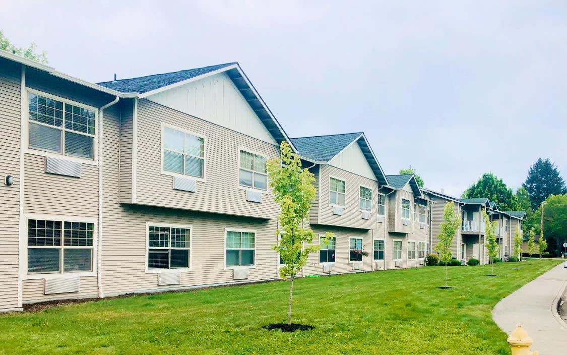 An exterior view of a residential apartment building with well-maintained lawns and young trees.