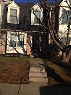 A brick residential house with a front yard and stairs leading to the entrance.