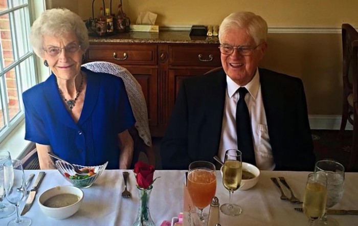An elderly couple dressed in formal attire enjoying a meal together, possibly celebrating a special occasion.