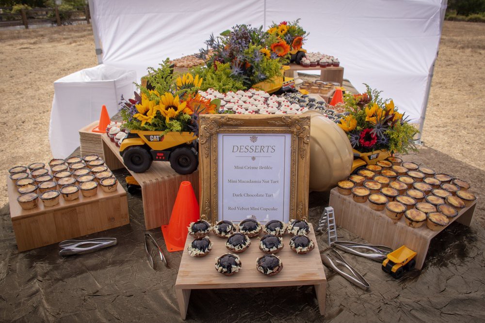 A rustic themed dessert table featuring cupcakes, vibrant flowers, and construction-themed decorations.