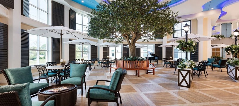 A spacious indoor lounge with comfortable seating, featuring a tree at the center and a piano.