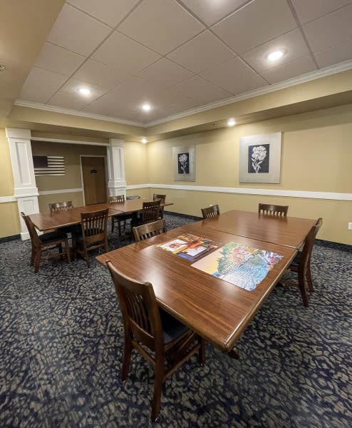 A well-lit conference room with wooden tables, chairs, and framed photos on the walls.