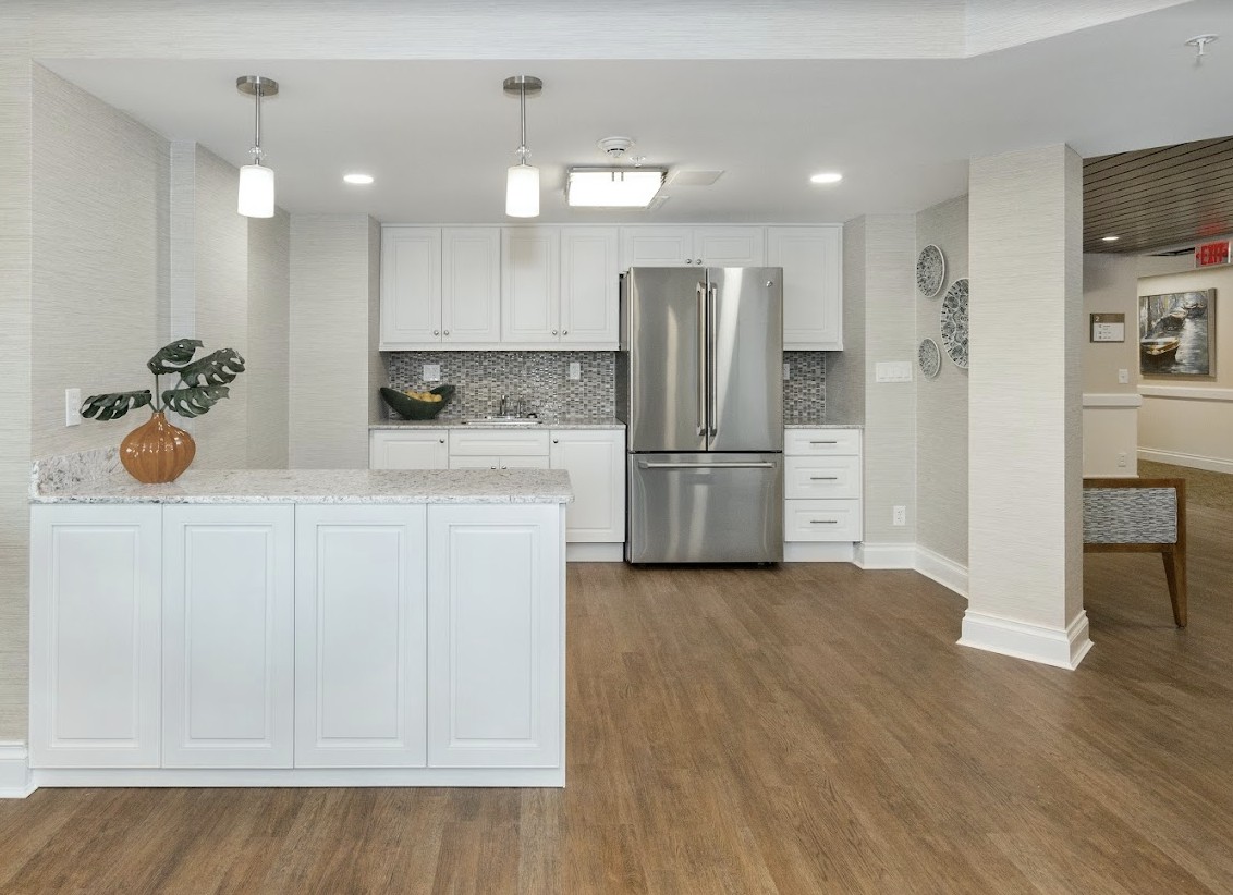 A modern kitchen with white cabinets, stainless steel appliances, and pendant lighting over a hardwood floor.