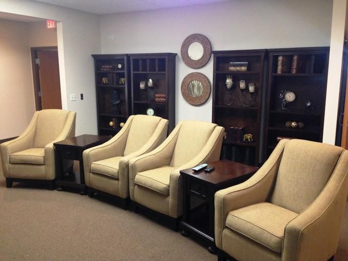 A waiting room with beige chairs and dark wood bookshelves.