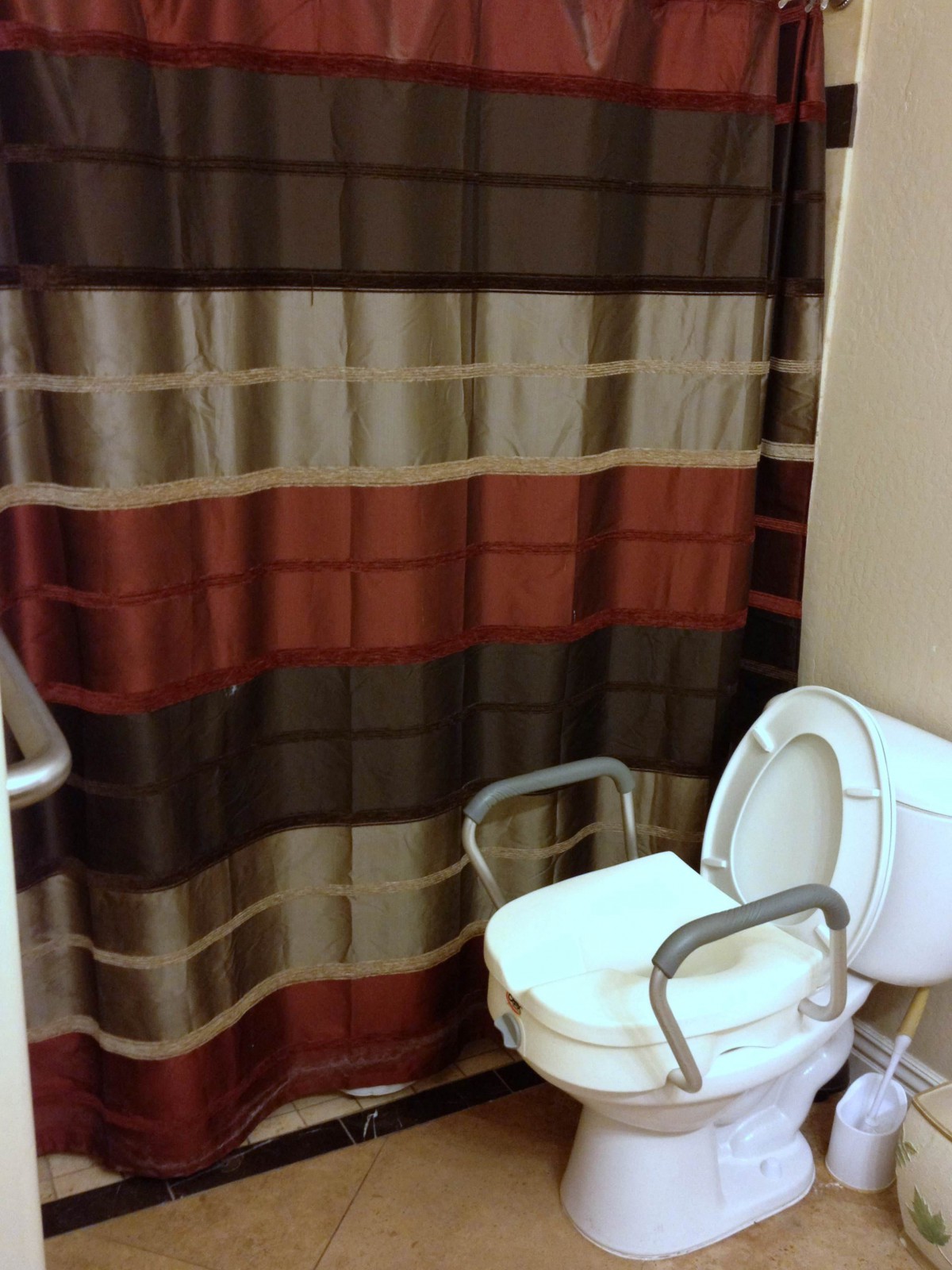 A bathroom featuring a colorful striped shower curtain and a toilet with safety bars.