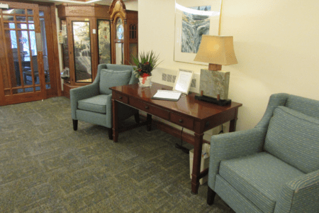 A cozy waiting room with two armchairs, a wooden table, and a lamp.
