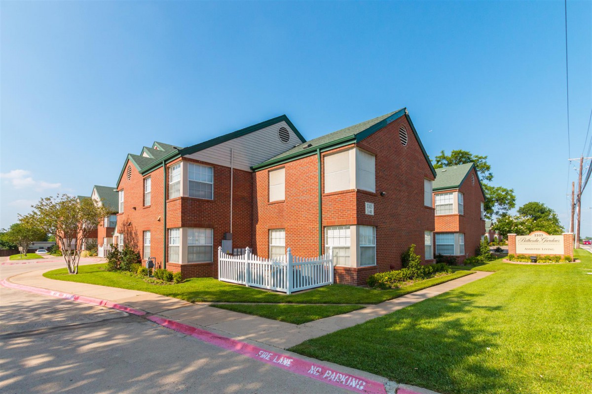 A two-story brick apartment building in a suburban neighborhood on a sunny day.