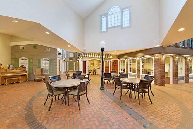 A spacious indoor dining area with round tables and chairs, featuring a brick floor and large windows.