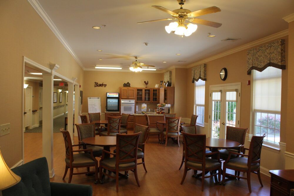 A cozy dining area featuring multiple tables and chairs, with a kitchen setup in the background and ceiling fans overhead.