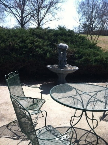 A serene outdoor patio featuring a fountain and metal chairs surrounded by lush greenery.
