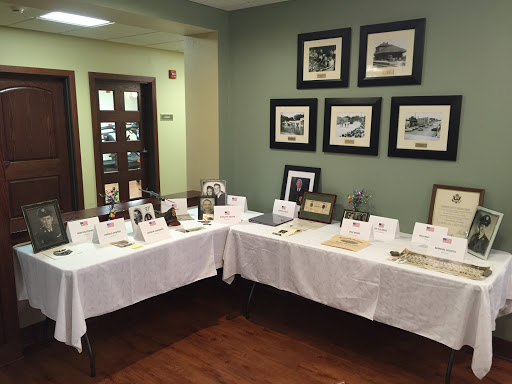A beautifully arranged exhibit featuring various items and photographs, displayed elegantly on white tables against a green wall.