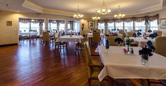 An elegant dining room with neatly arranged tables and chairs, featuring chandeliers and wooden flooring.