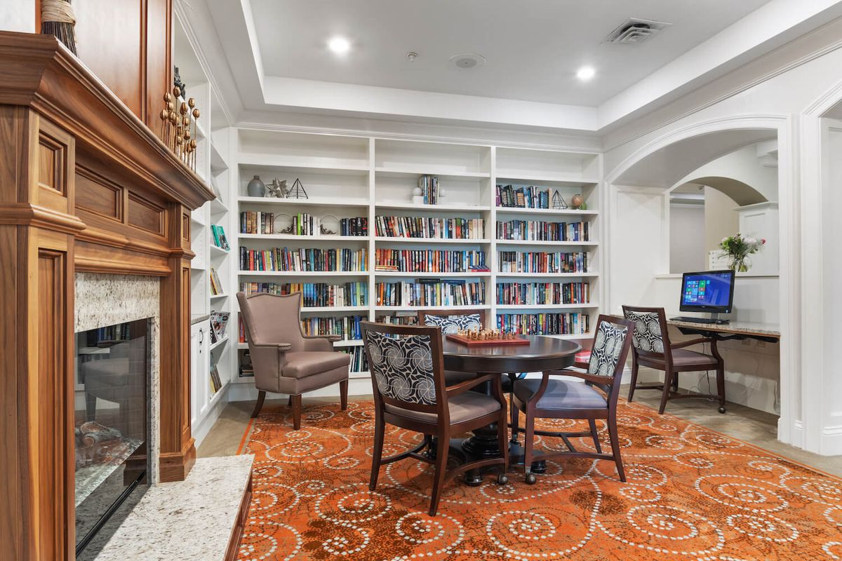 A cozy library with bookshelves, comfortable chairs, and a fireplace.