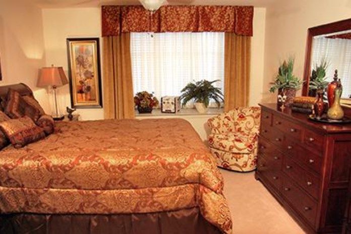 A cozy bedroom with warm decor, featuring a bed, dresser, and window with curtains.