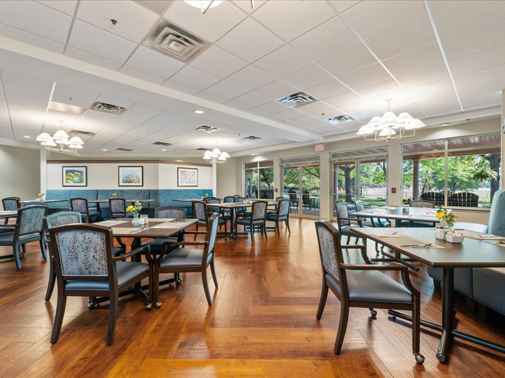 An inviting dining area with neatly arranged tables and chairs, illuminated by soft lighting and complemented by warm wood flooring.