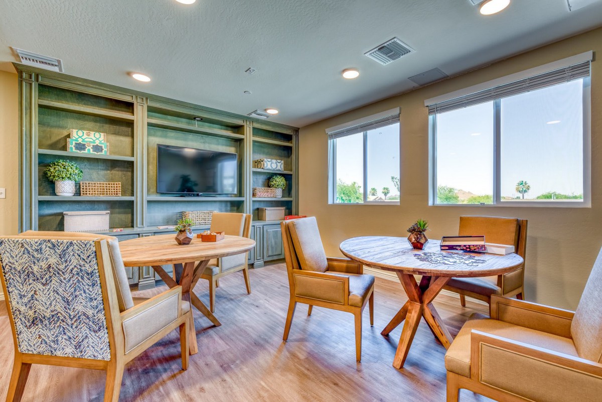 A modern room with wooden tables and chairs, featuring large windows and built-in shelves.