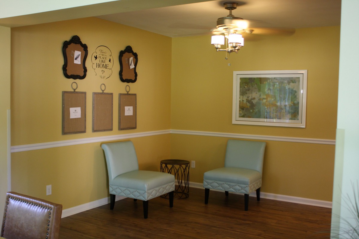 A cozy living room with yellow walls, featuring two chairs, wall art, and a ceiling fan.