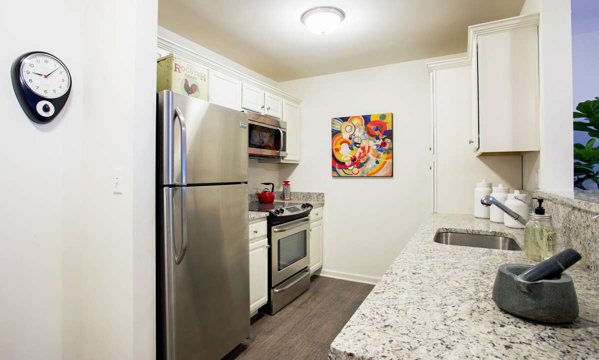 A modern kitchen with stainless steel appliances and white cabinets, featuring colorful artwork on the wall.