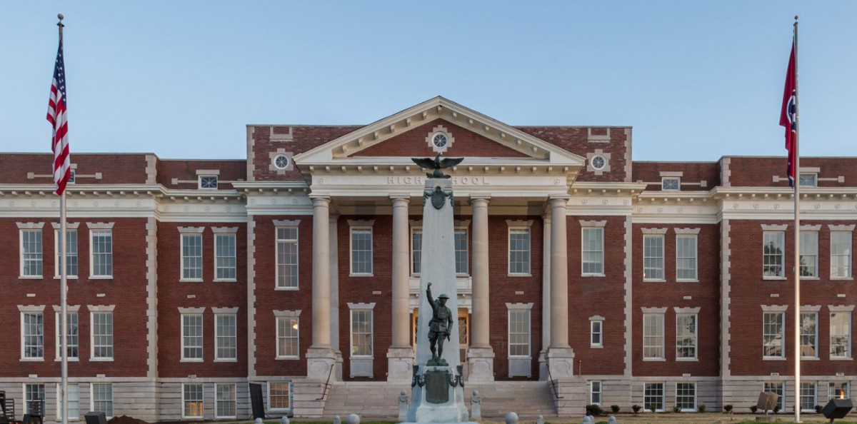 A historical building with classical architecture featuring large columns and a prominent monument in front.