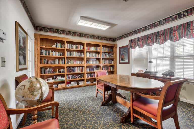 A cozy library room with bookshelves, a large table, and chairs.