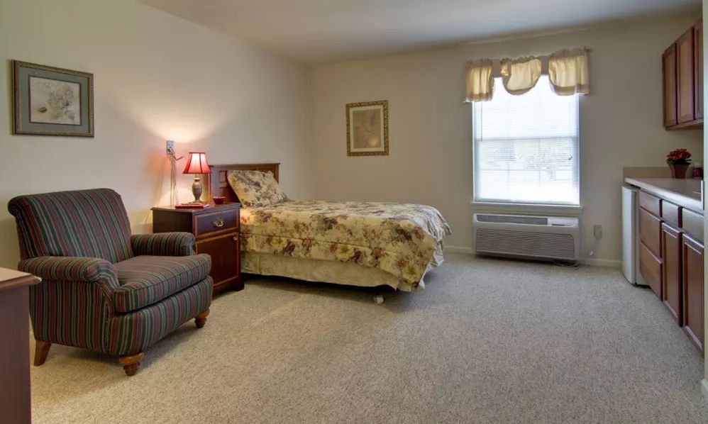 A cozy bedroom with a single bed, armchair, and a large window.