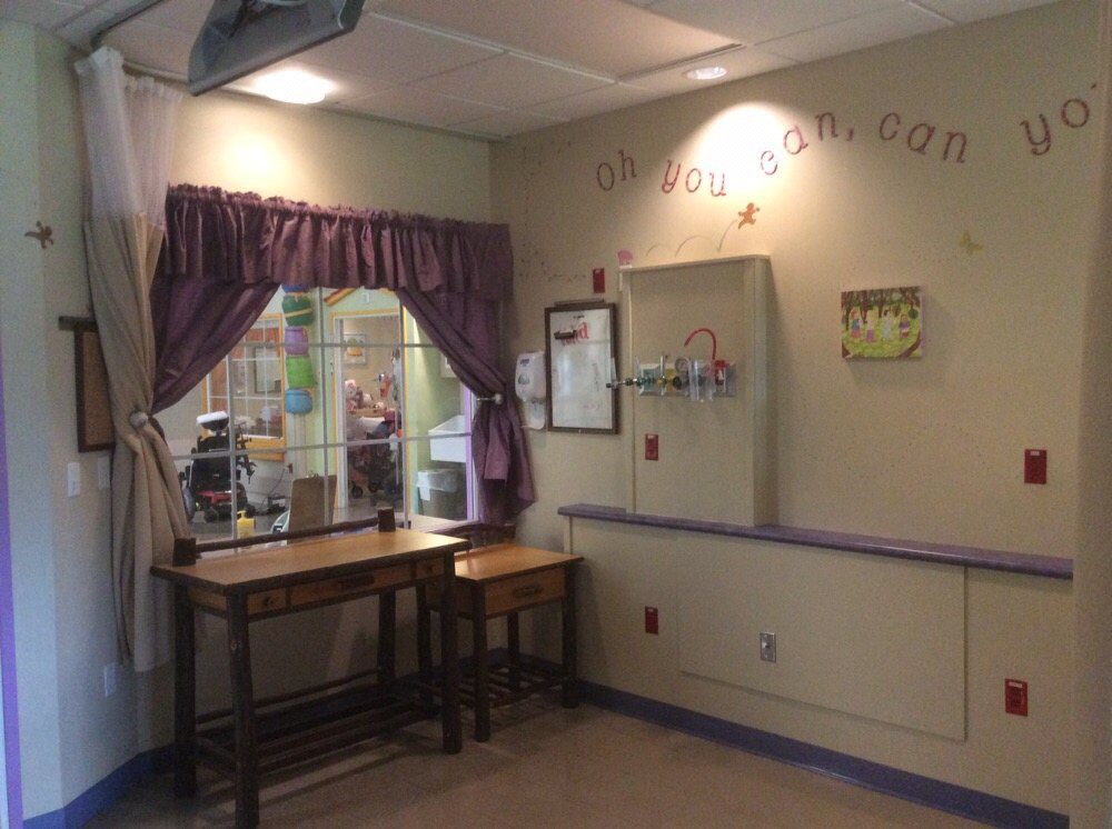 A cozy waiting area in a children's hospital with a table, chairs, and purple curtains.