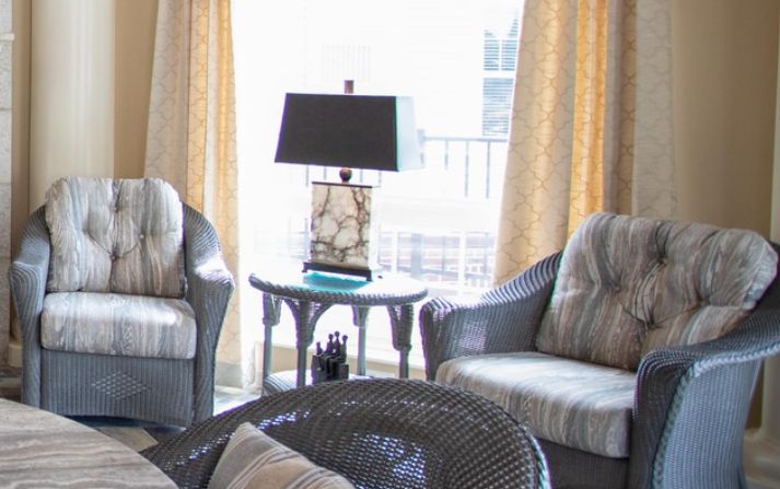 A cozy living room setup with cushioned chairs and a lamp on a side table near a window with curtains.