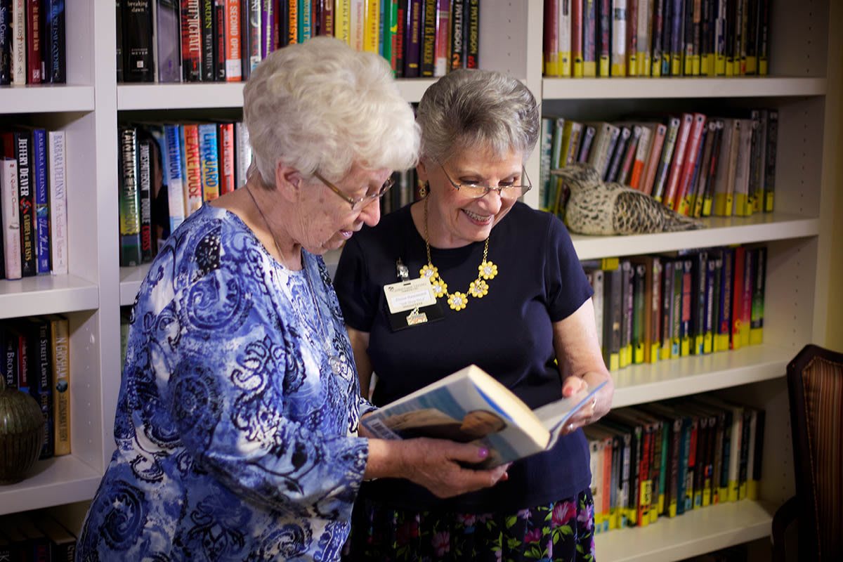 Two women discussing a book in a library setting.