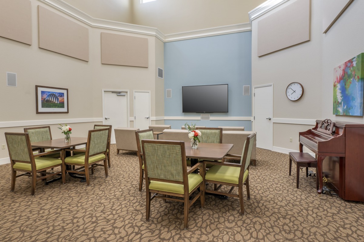 A communal dining area with tables and chairs, featuring a television and wall clock.