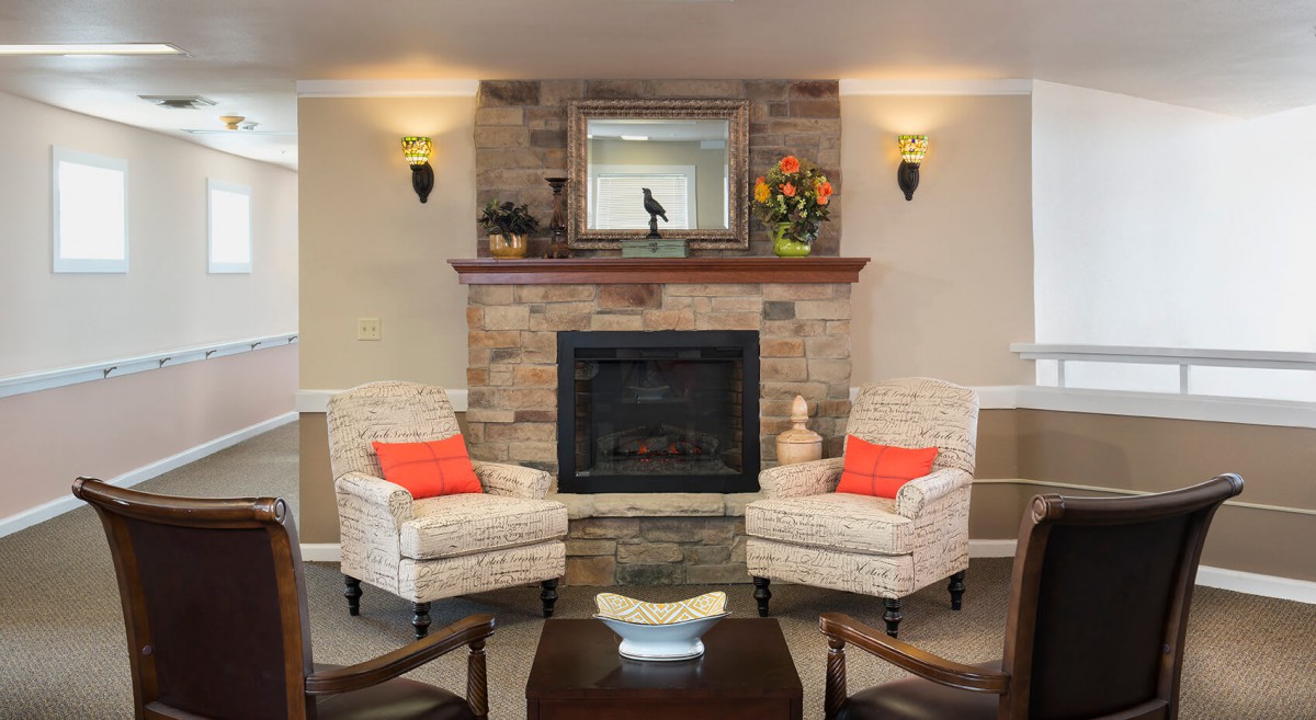 A cozy living room with a stone fireplace, mirrored mantle, and two armchairs adorned with orange cushions.