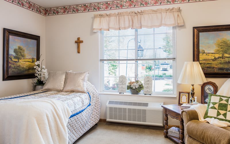 A cozy bedroom with a bed, decorative pillows, and a window with floral curtains.
